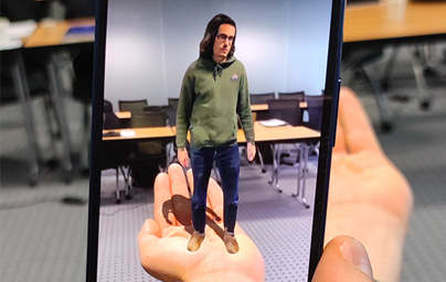 smartphone visant une main tendue avec incrustation en temps réel d'une personne miniaturisée dedans